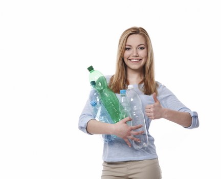 A young woman with long, straight red hair, wearing a light blue long-sleeve shirt and beige trousers, stands against a plain white background. She is smiling and holding a bundle of clear and green recycling bottles in her arms, which include plastic soda and water bottles of different shapes and sizes. Her right hand is giving a thumbs-up gesture, indicating satisfaction or approval. The scene conveys an environmentally conscious attitude and a focus on waste recycling, relevant to rubbish removal services in Tufnell Park. The lighting is bright and even, emphasizing the clarity of the bottles and her cheerful expression. This image is suitable for a website section highlighting eco-friendly waste disposal, demonstrating the careful handling of plastic recyclables, which aligns with the services provided by Garden Clearance Tufnell Park in managing household rubbish and clutter removal effectively.